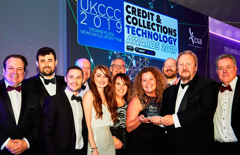 CCICM Director Carl Hackman (centre right) and Consumer Collections manager Heulwen Jones (centre left) hold the CSA CAI Award, watched by many of CCICM’s senior managers and collectors, and joined by CSA President John Ricketts (far right) and TV actor Shaun Williamson (far left). Credit: Hannah Taylor, The Lens Box.